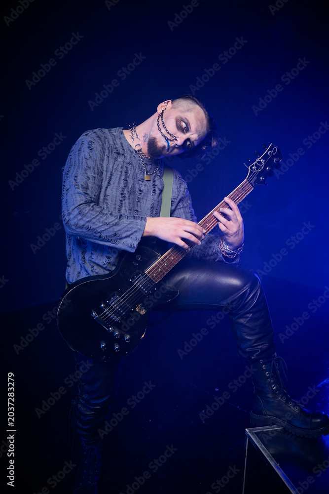 Fototapeta premium Young man with skeletal face paint playing electric guitar in dark moody setting