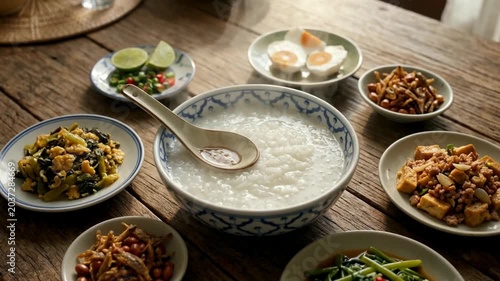 A traditional meal featuring a large bowl of rice porridge surrounded by various side dishes on a wooden table