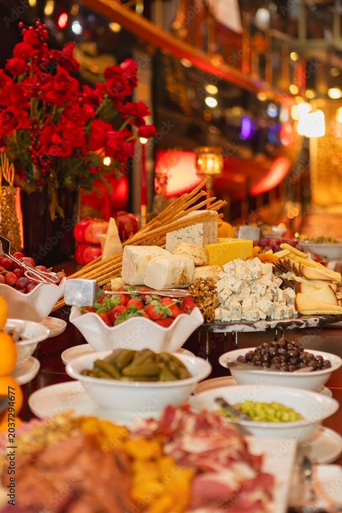 Fototapeta premium A banquet spread of assorted cheese, breadsticks, strawberries, olives and fruit elegantly arranged for an evening event