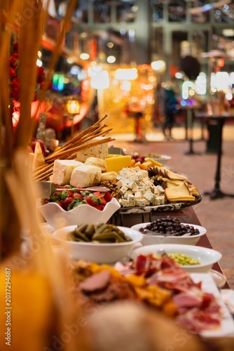 A long buffet table lined with cheese boards, charcuterie, olives, dolma, strawberries, and breadsticks at an elegant indoor evening event.