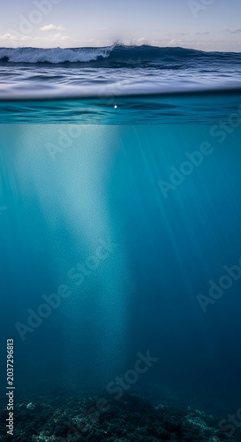 Split shot of a breaking ocean wave above and a sunlit underwater scene with rocky bottom, symbolizing adventure and the duality of nature.