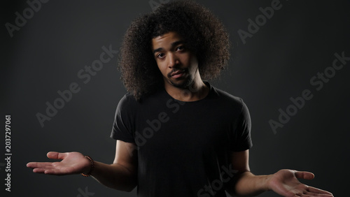 Foto Young man with afro hair shrugging, showing doubt and questioning with open hand