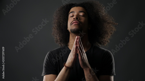 Young man with afro hair closing eyes, having his hands in a prayer position