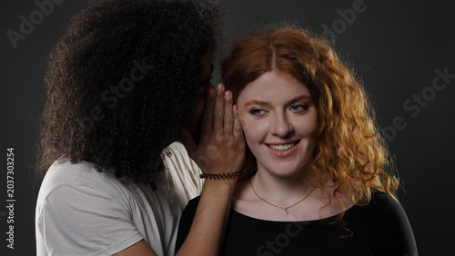 Young man whispering a secret into the ear of a young woman smiling