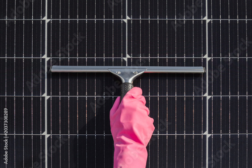 Tableau sur toile Woman hand in pink rubber protective glove holding squeegee with rubber blade and cleaning dark black solar panels