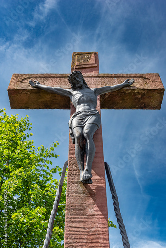 Wegkreuz aus Sandstein mit gekreuzigtem Jesus in extremer Unteransicht mit blauem Himmel