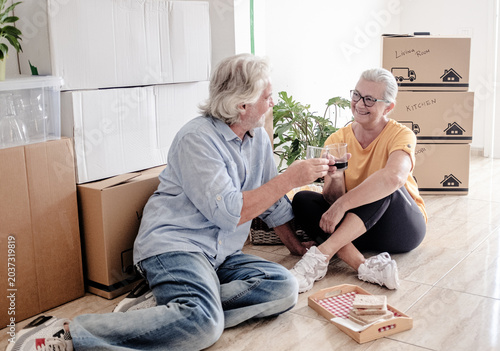 Canvastavla An elderly couple moving into a new home, sitting on the floor for a break and a toast surrounded by moving boxes in an empty room