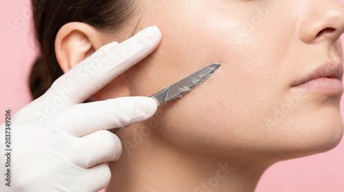 Cosmetologist performing dermaplaning facial exfoliation with scalpel on woman