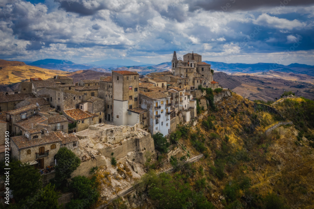 Naklejka premium Aerial drone view of town Petralia Soprana, Sicily, Italy. An avenue of trees leading to the hilltop in the Madonie Mountains. August 2024