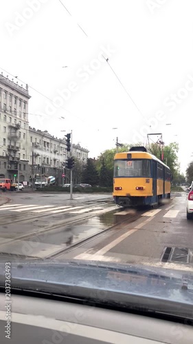 A city tram drives through puddles after a rainstorm. Shot through a car's windshield