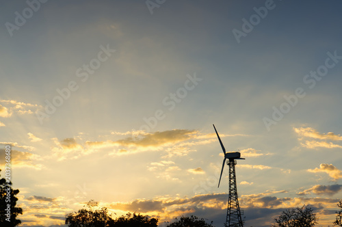 Silhouette of a wind turbine for renewable energy against a beautiful golden sunset sky with sunrays.