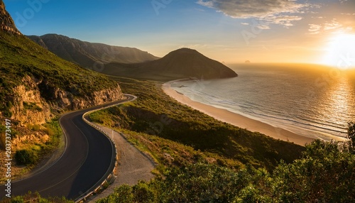 Scenic Mountain Road Winding Towards A Beach At Sunset