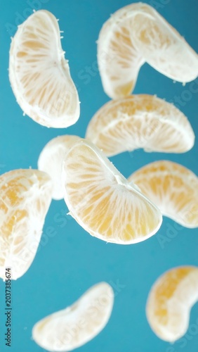 Fresh mandarin orange segments falling in motion against a bright vibrant teal blue background studio photography