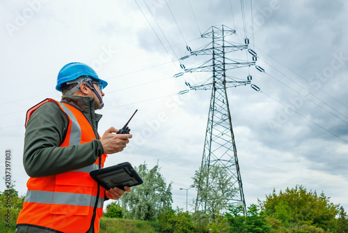 Side view of a male electrical engineer working near a high-voltage power line. Technician or power inspector inspects the power grid infrastructure.