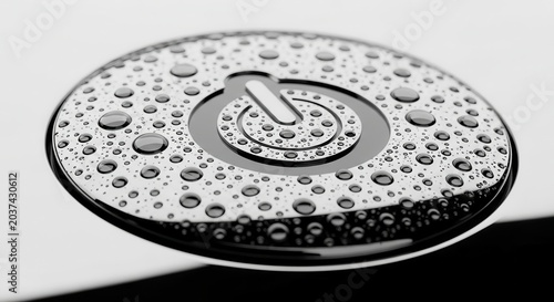 Close-up of a power button symbol covered in water droplets on a metallic surface.