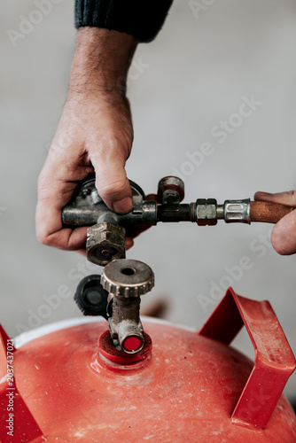 craftsman is replacing an empty red gas cylinder on a gas burner
