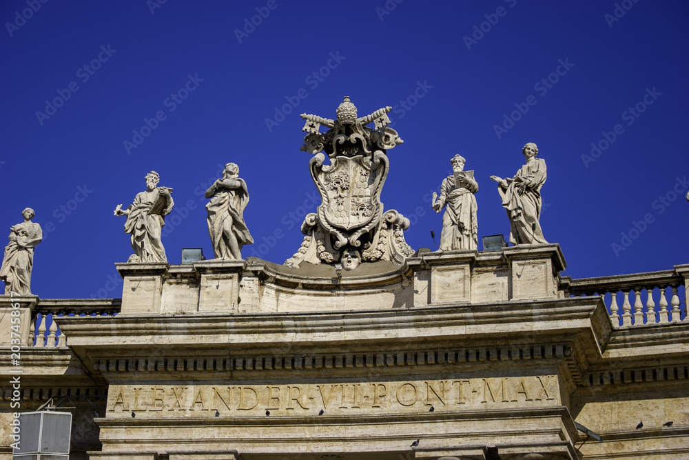 Obraz premium Statues of saints line the colonnade of St. Peter's Square in Vatican City under a clear blue sky.