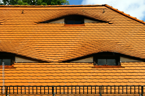 Wavy terracotta roof with curved dormer windows on whimsical architectural house facade