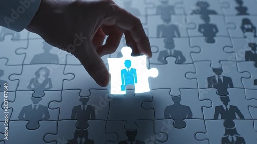 Close-up of a hand placing a glowing puzzle piece with a human figure into a larger puzzle with many similar pieces, conveying a technological and problem-solving concept.