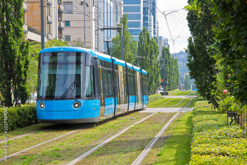 MODERN BLUE TRAM ON GREEN TRACK IN URBAN CITYSCAPE - Eco friendly public transport with electric tram, sustainable mobility, commuting and urban travel concept - Europe, Norway, Oslo