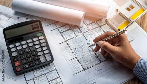 hand using calculator over construction plans and financial paperwork for budget planning