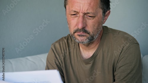 Middle-aged man reading important document looking worried and thoughtful at home, 4K