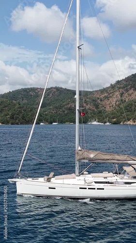 Sailing yacht glides across calm blue sea near verdant, hilly coastline