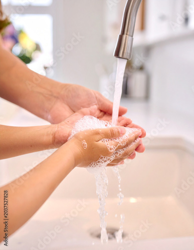 The mother guides her child in washing hands after gardening, focusing on soap bubbles and running water.