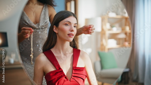 Two women proposing jewelry to friend looking mirror wearing red dress closeup.