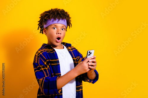 фотографія Surprised boy holding smartphone against bright yellow background reacting to a
