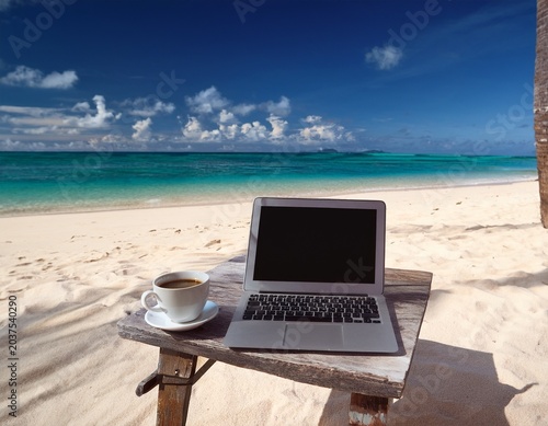 working remotely with a laptop and coffee on a sunny beach in a tropical paradise