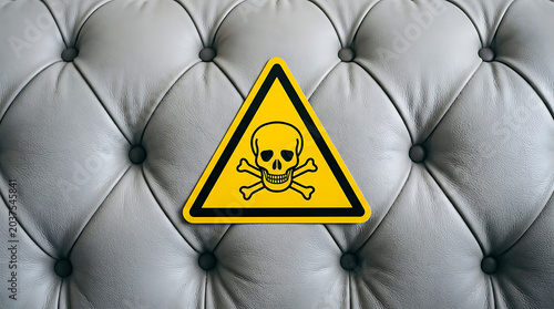 Prominent yellow hazard sign with skull and crossbones symbol against a textured tufted background, indicating danger