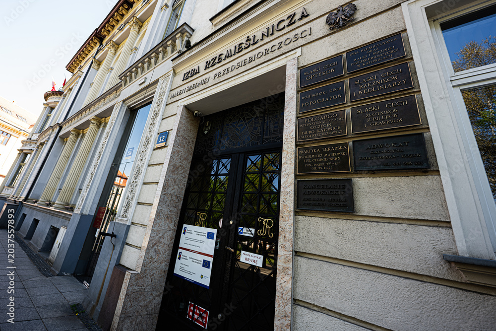 Naklejka premium Historic craft chamber entrance with ornate plaques and classical facade in Katowice, Poland showing signage, office names and urban architecture on a slanted street perspective