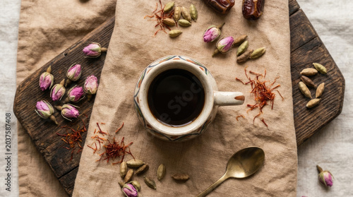 Rich coffee served in decorative cup, surrounded by rosebuds, cardamom, and saffron