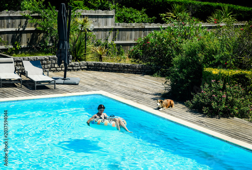 Beautiful young girl enjoying relaxing in the pool during a heatwave with her dog