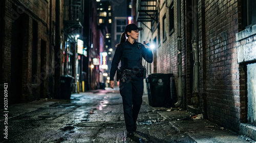 Female Police Officer Patrolling Dark City Alleyway at Night with Flashlight