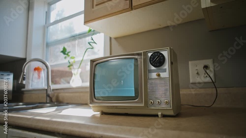 In a quaint kitchen, an old-fashioned retro TV displays black and white static. The warm atmosphere invites viewers to reminisce about the charm of past technology