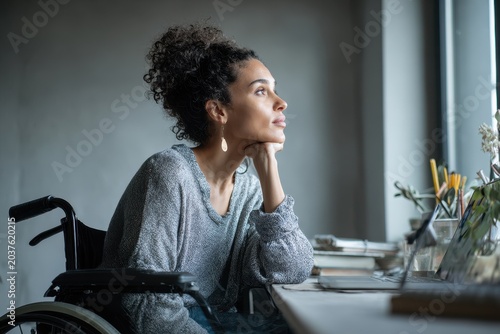 Portrait of a wheelchair user working remotely in a clean grey-toned home workspace with copy space