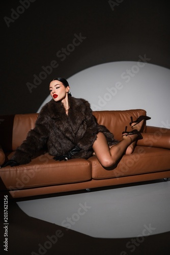 Elegant Woman Posing. Glamorous Woman Lounges Confidently On Leather Couch With Intense Cinematic Lighting