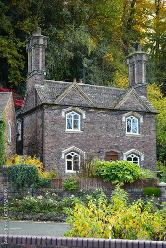 Charming Old Brick Cottage With White Windows Surrounded By Vibrant Autumn Foliage In Ironbridge, Shropshire, England.