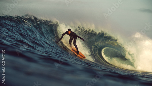 surfer taking off on big tubular wave at sunrise