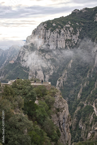 Tourists admire the dramatic landscape from a viewpoint on the rugged cliffs of Montserrat mountain in Catalonia, Spain