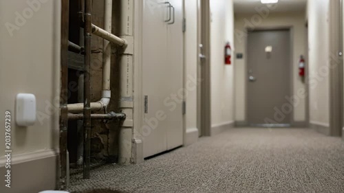 Medium shot of IoT sensors detecting water leaks in an apartment hallway with blurred pipes and walls in the background for smartbuilding risk monitoring.