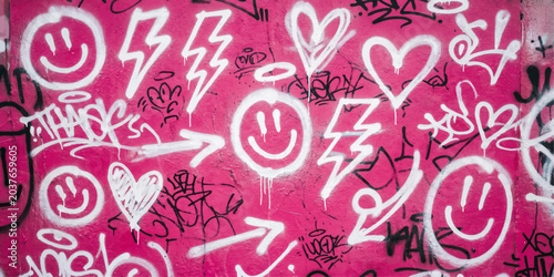 Schilderij op canvas Graffiti of Smiley Faces and Hearts on Pink Wall: A vibrant collage of white graffiti featuring smiley faces, hearts, and lightning bolts adorns a pink wall