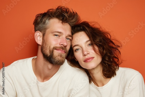 Portrait of a glad caucasian couple in their 30s wearing a simple cotton shirt isolated in pastel orange background