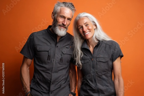 Portrait of a happy couple in their 60s sporting a technical climbing shirt on soft orange background
