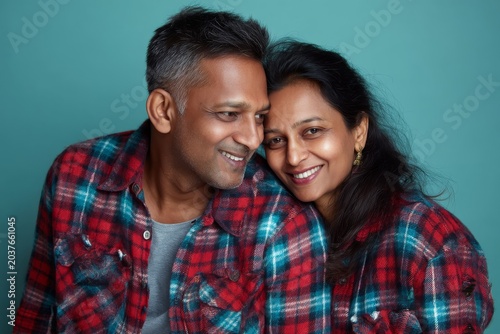 Portrait of a blissful indian couple in their 40s wearing a comfy flannel shirt in soft teal background