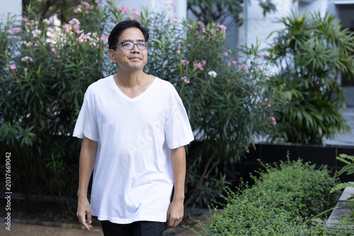 Relaxed happy carefree middle age old Asian man taking evening walk, breathing the clean, unpolluted air in green park, wellness concept image of good summer, summer wellness