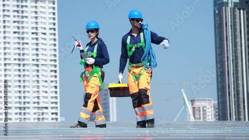 Workers inspecting renewable energy station on building roof, Professional technical team discussing maintenance of solar panel system, Engineers in safety uniform walking on solar rooftop