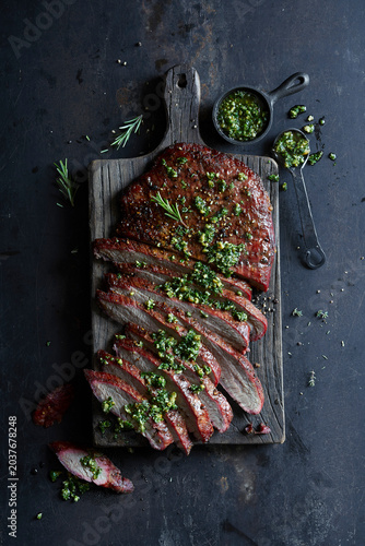 Sliced grilled flank steak topped with fresh chimichurri on a rustic wooden board.